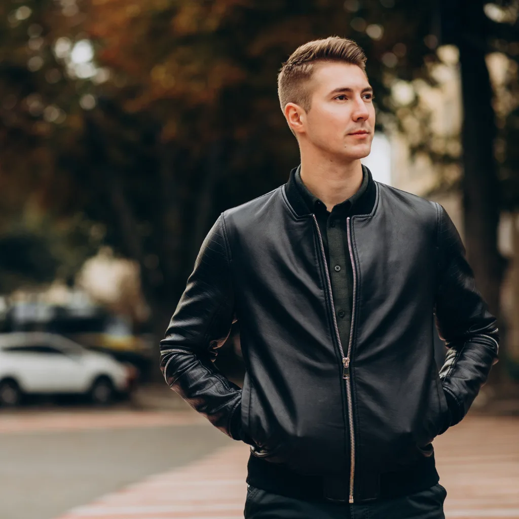 Man in a black leather jacket on a city street lined with autumn trees