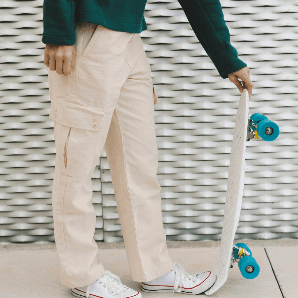 Person in cream cargo pants and white sneakers holding a skateboard
