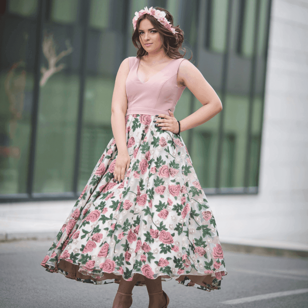 Woman in a pink top and a full floral midi skirt standing in front of a glass building
