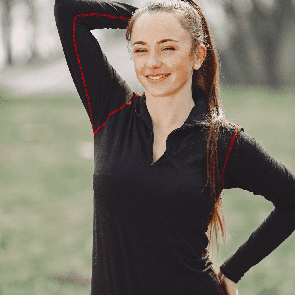 Smiling woman in a black half-zip long-sleeve top with red trim, standing outdoors with one hand on her hip