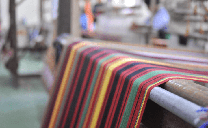 Close-up of striped fabric in red, green and yellow being woven on a loom