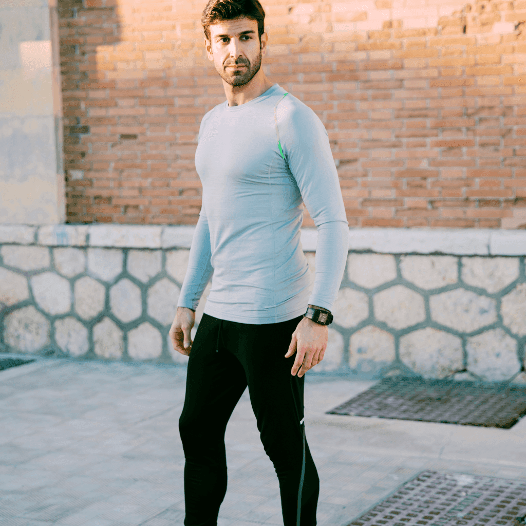 Man in a pale blue long-sleeve top and black training tights in front of a brick wall